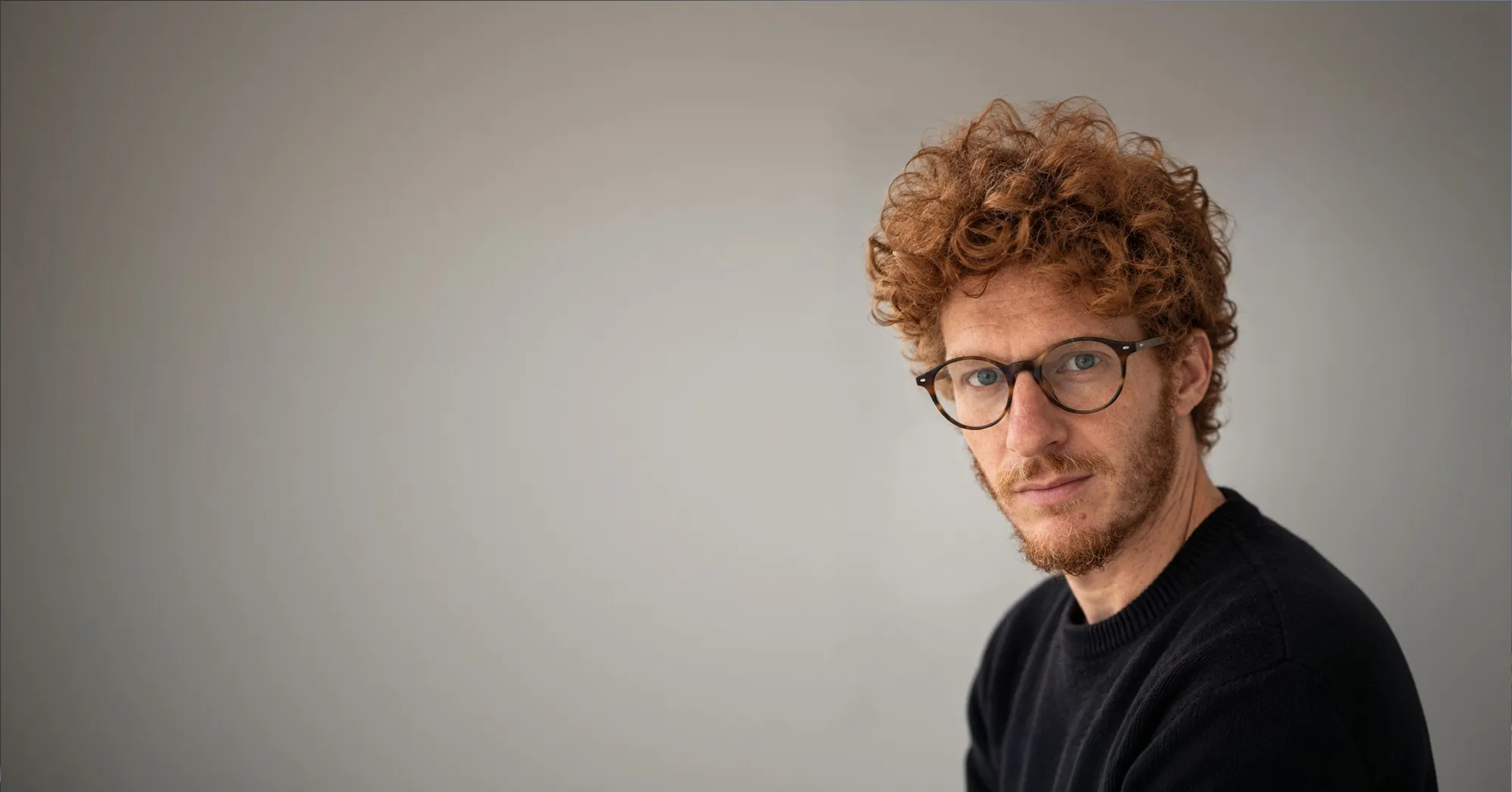 Ritratto di Loris Rigoni, con occhiali e maglione scuro su fondo grigio